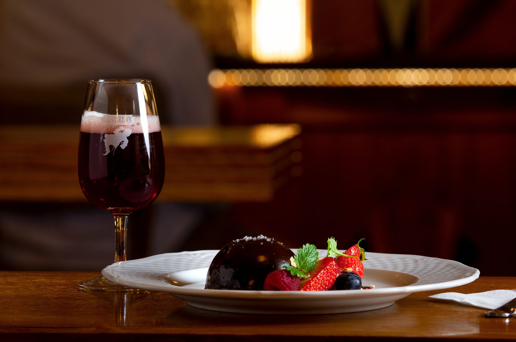 Chokladdessert med jordgubbar, blåbär och mynta bredvid ett glas mörk röd öl