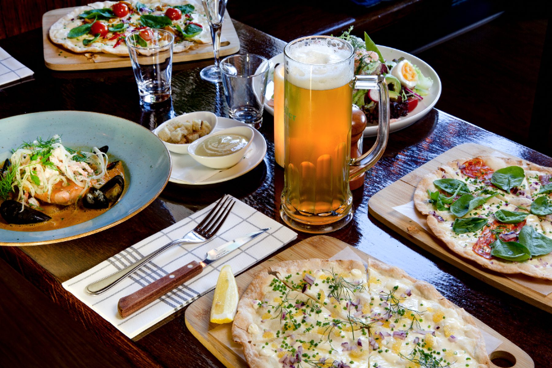 Bord med två flammkuchen, en skål fiskgryta med musslor och lax, sallad och en hög sejdel ljus öl