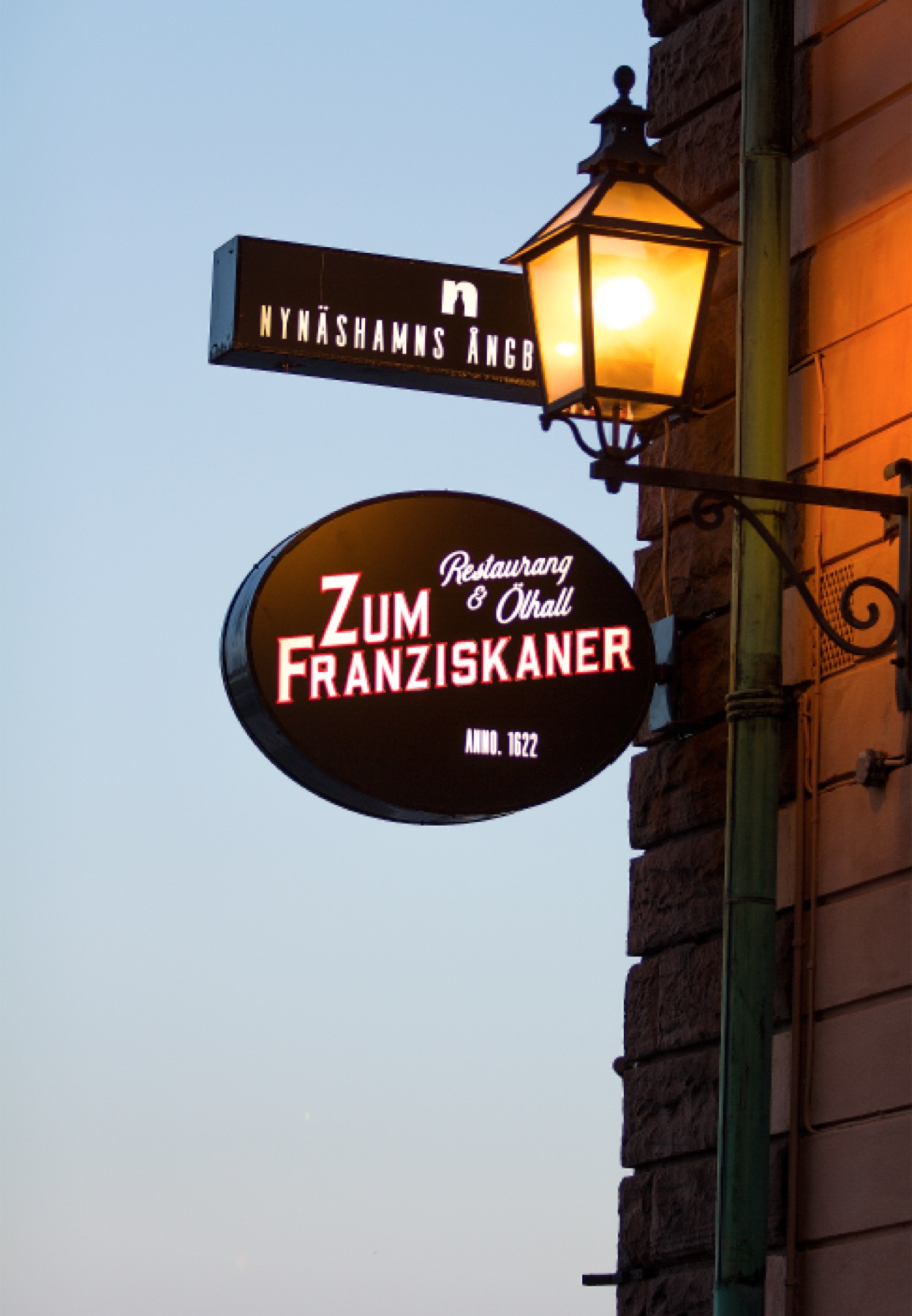 Den ovala skylten Zum Franziskaner Restaurang och Ölhall under en gaslykta på fasaden