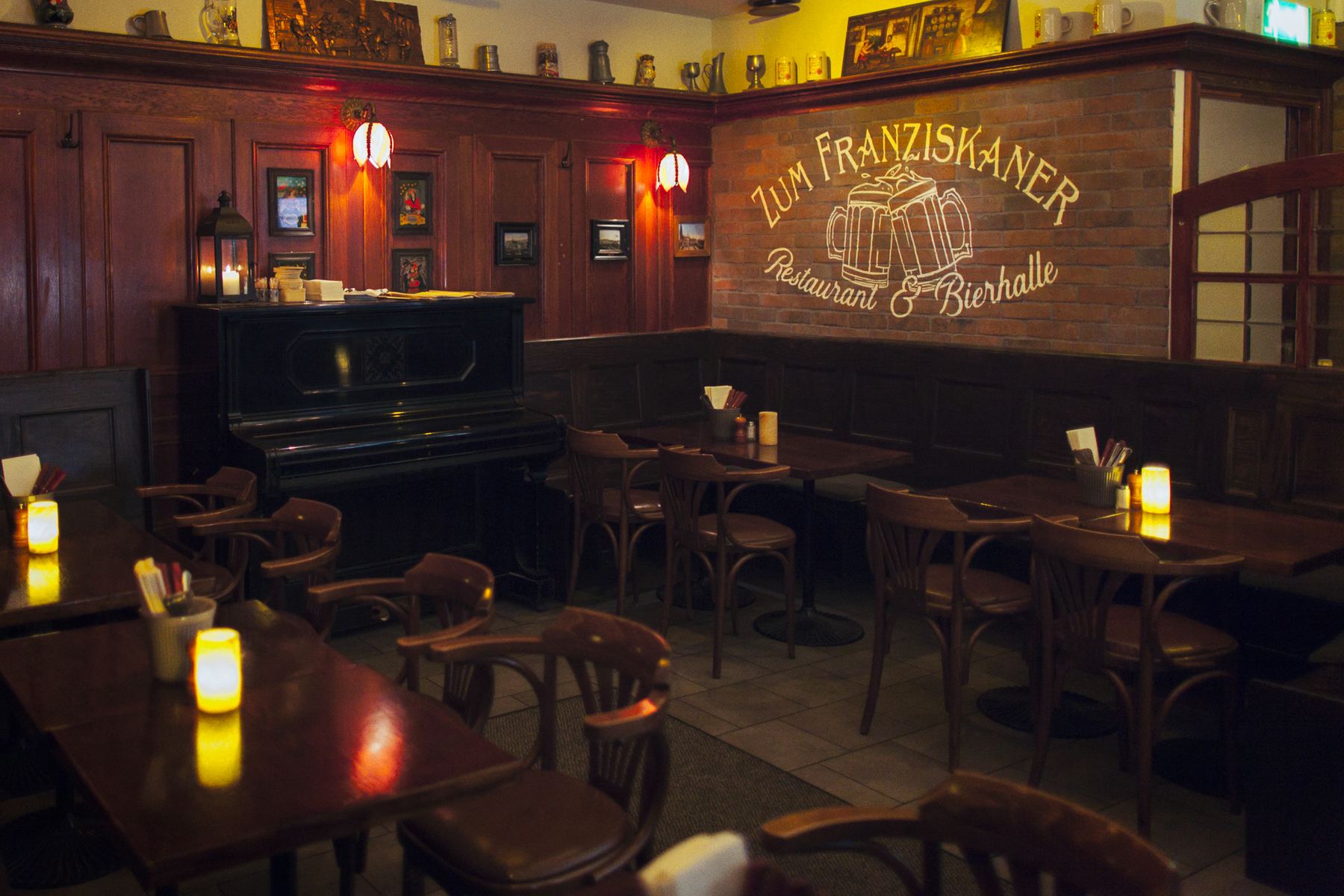 Ölhallen med träpanel i mörk ek, den målade skylten Zum Franziskaner Restaurant och Bierhalle på väggen och levande ljus på borden